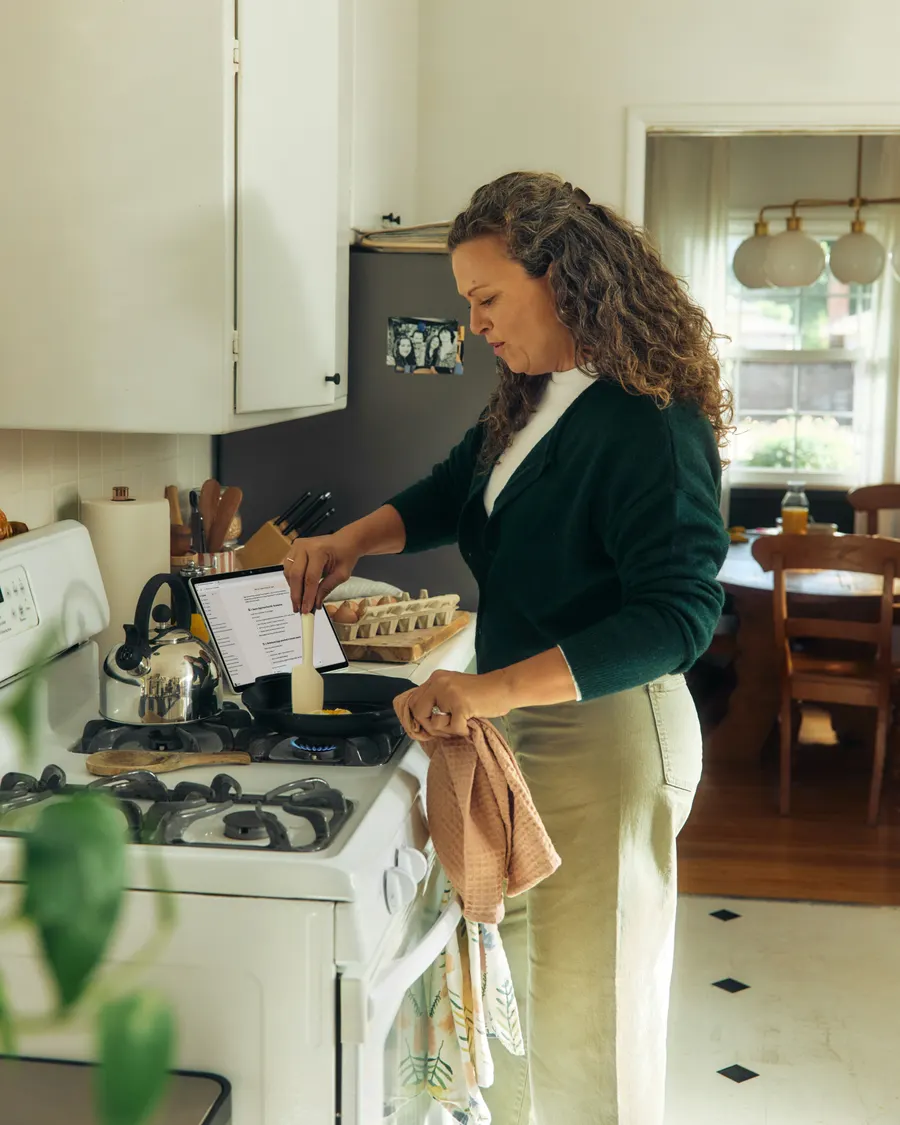 A mother in her own kitchen, cooking one egg in a small pan, a tea towel over her arm.